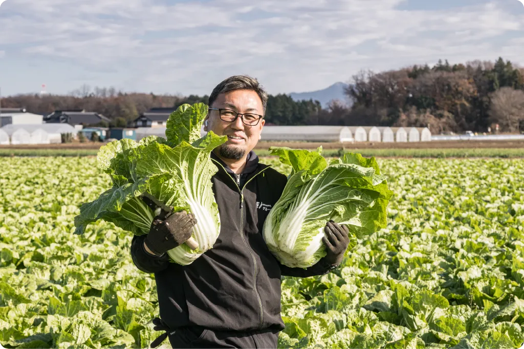 白菜を両手に畑に立つ生産者